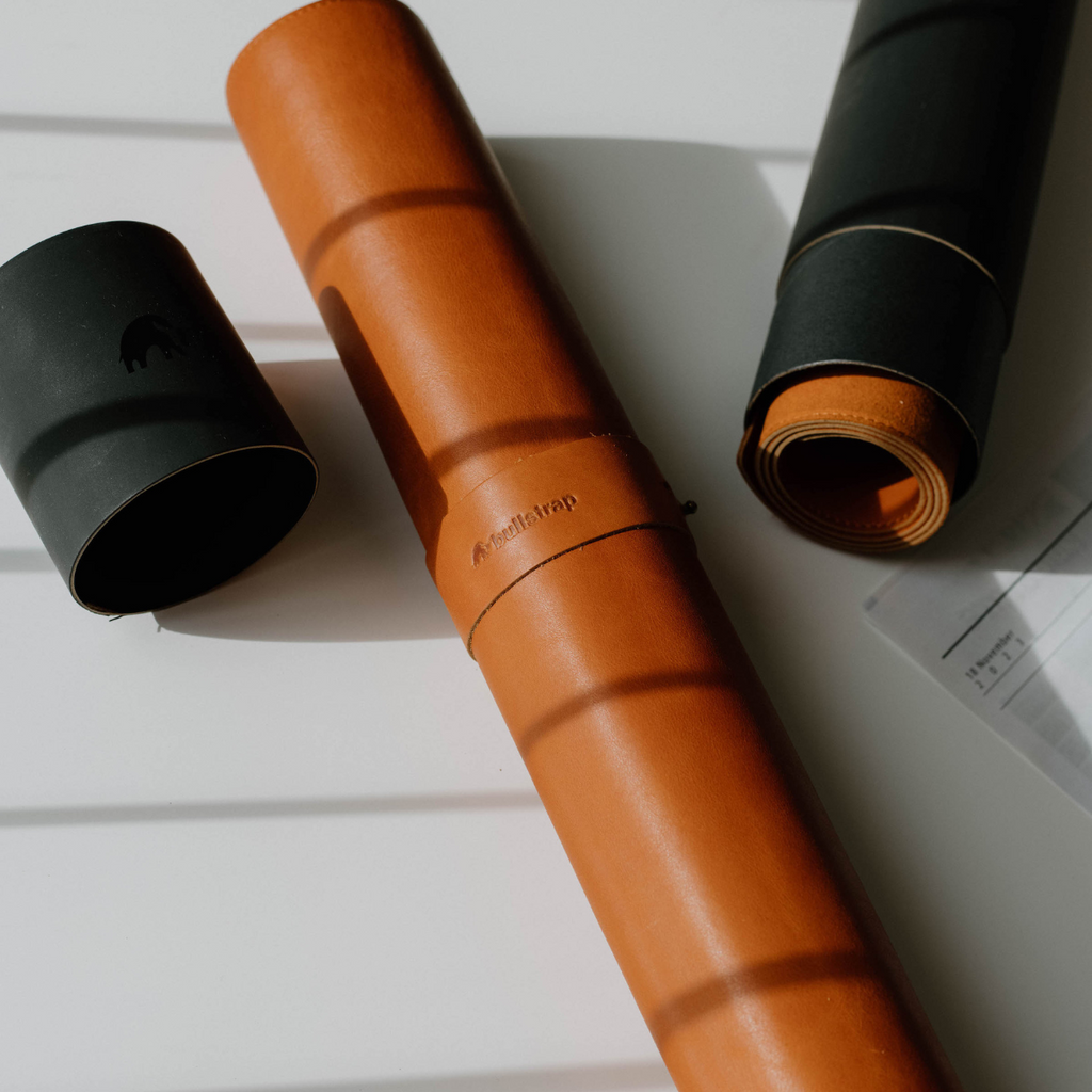 Rolled leather desk mat in sienna color with black leather wraps and a logo visible
