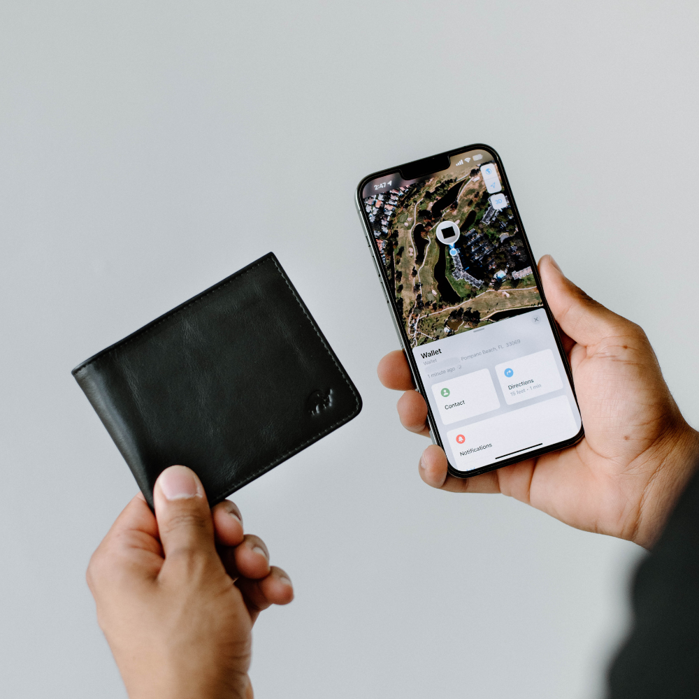 A person holding a black leather bifold wallet and a smartphone displaying a map.