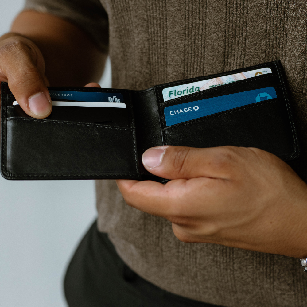A person holding a black leather bifold wallet open, showing card slots with cards inside.