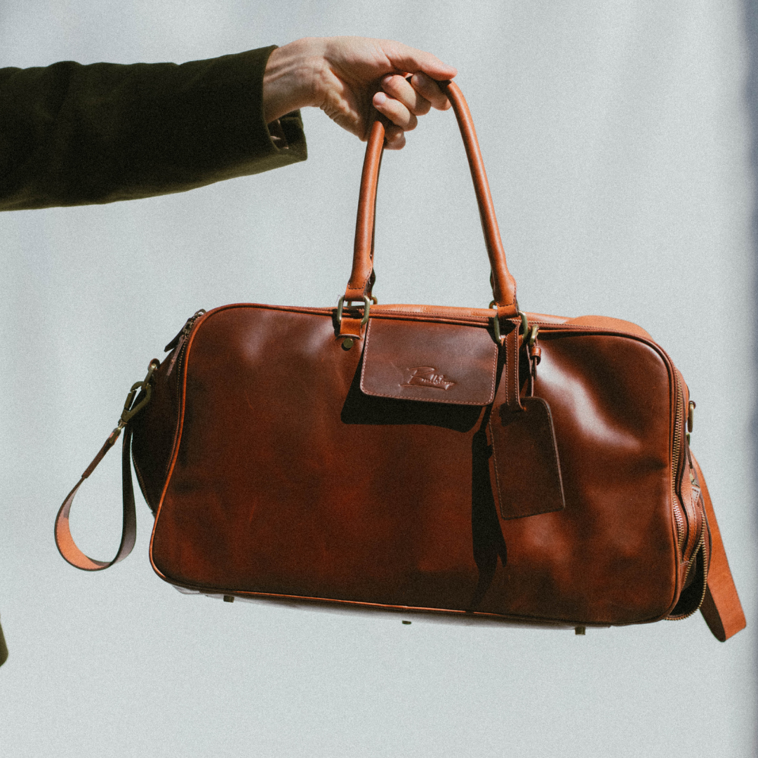 Front view of Bullstrap Reserve Odyssey travel bag in brown leather with top handles, detachable strap, and luggage tag