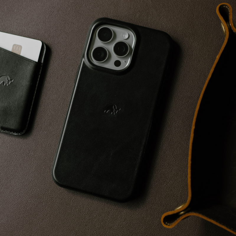 Black leather iPhone case next to a card holder on a brown surface.