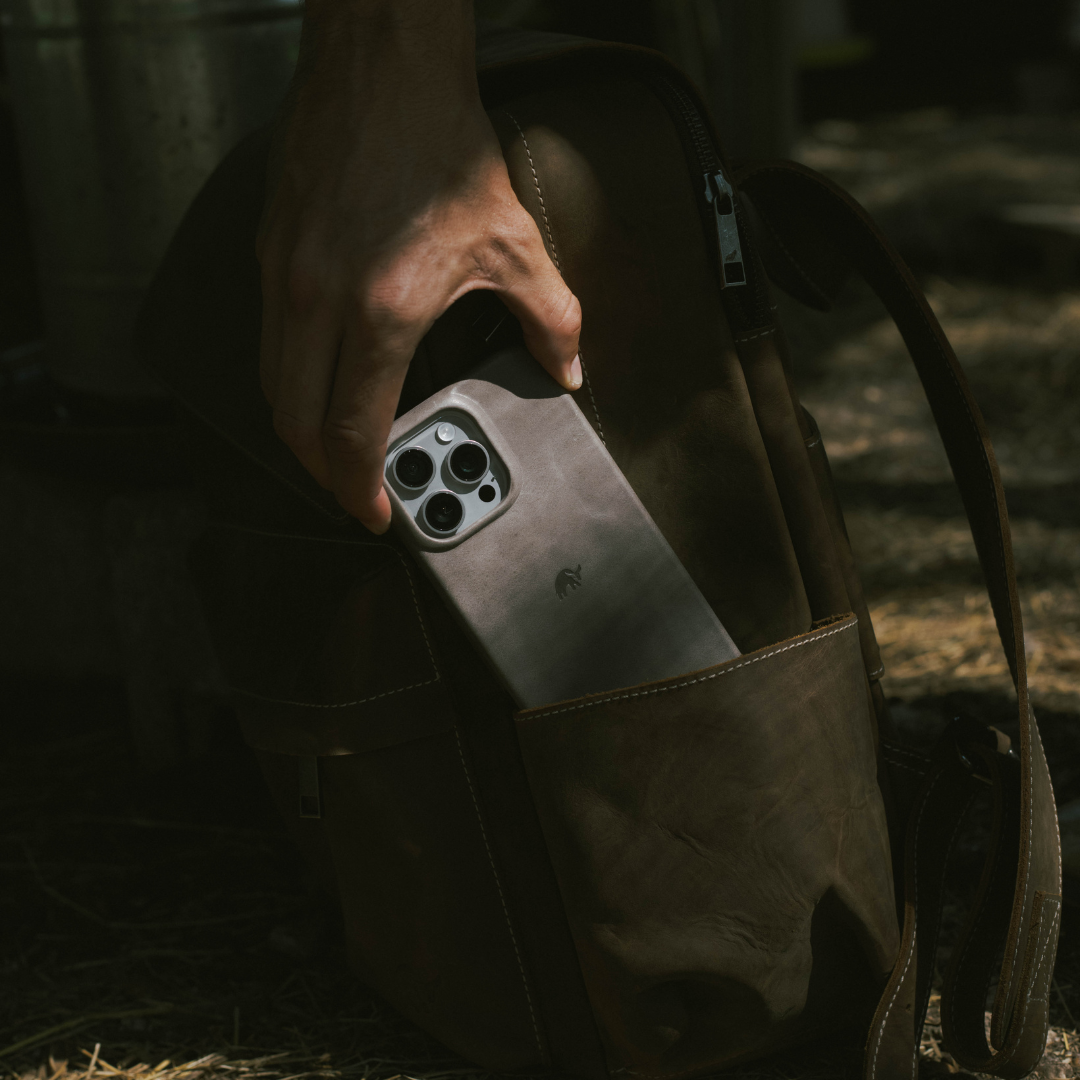 Hand sliding a phone in a slate-gray minimalist leather case into a brown leather bag pocket