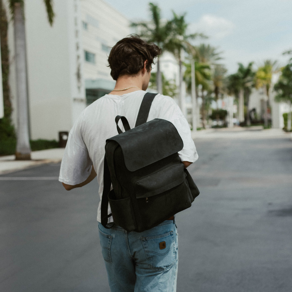 Person walking away down a palm-lined urban street wearing a white T-shirt, blue jeans and a black backpack