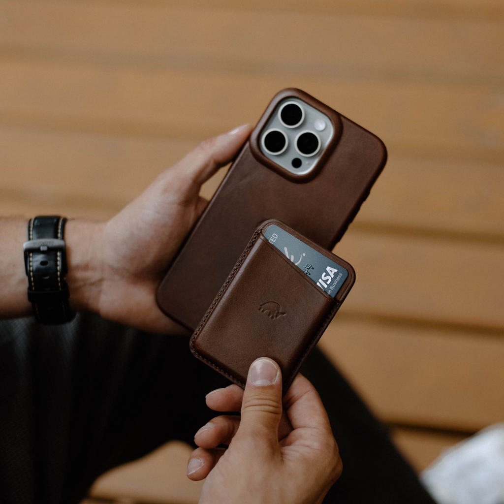 A person holding a brown leather wallet and a phone, with a card visible in the wallet.