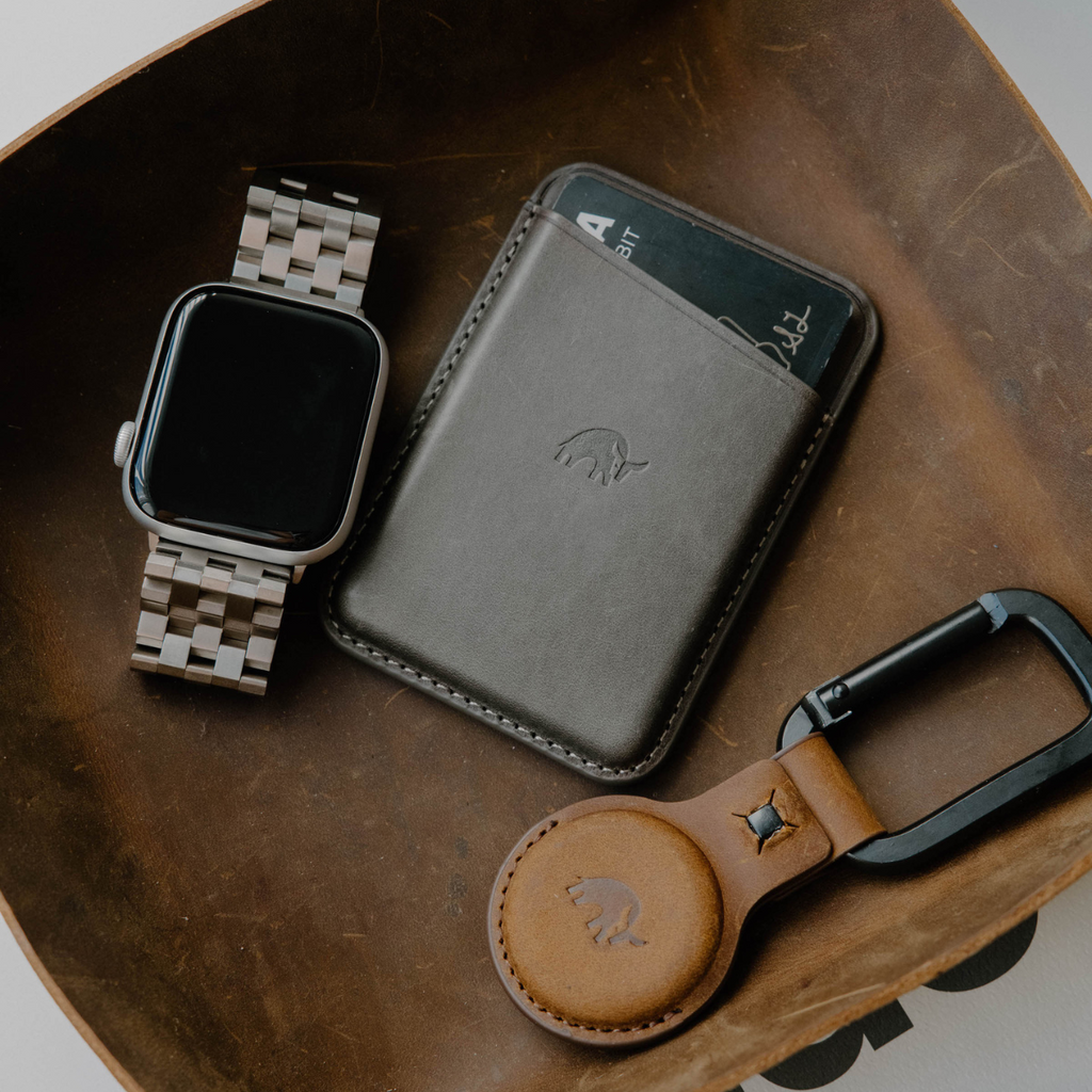 Leather Magnetic Wallet in slate color, placed with a watch and keychain on a wooden tray.