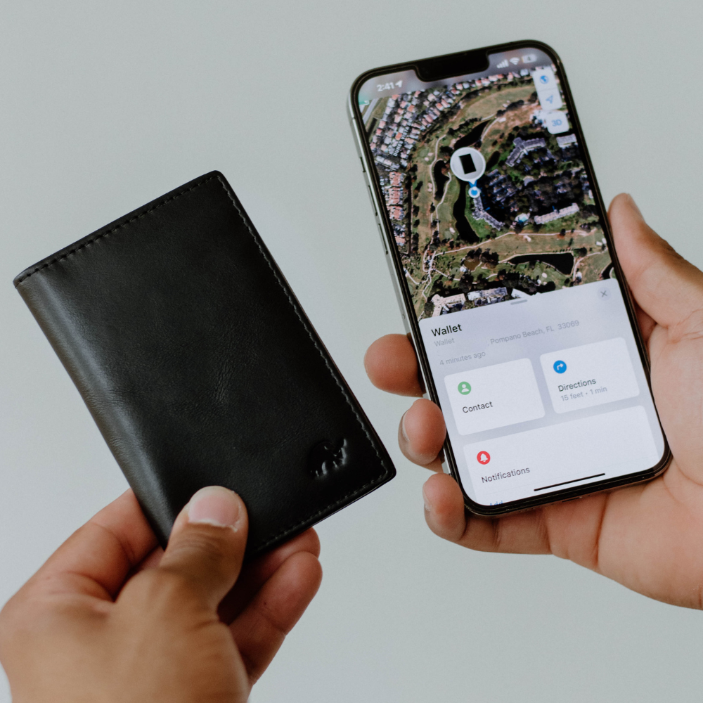A person holding a black leather wallet next to a phone displaying a map with wallet information.