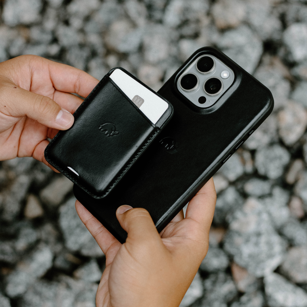 A person holding a black leather phone case and a matching wallet.