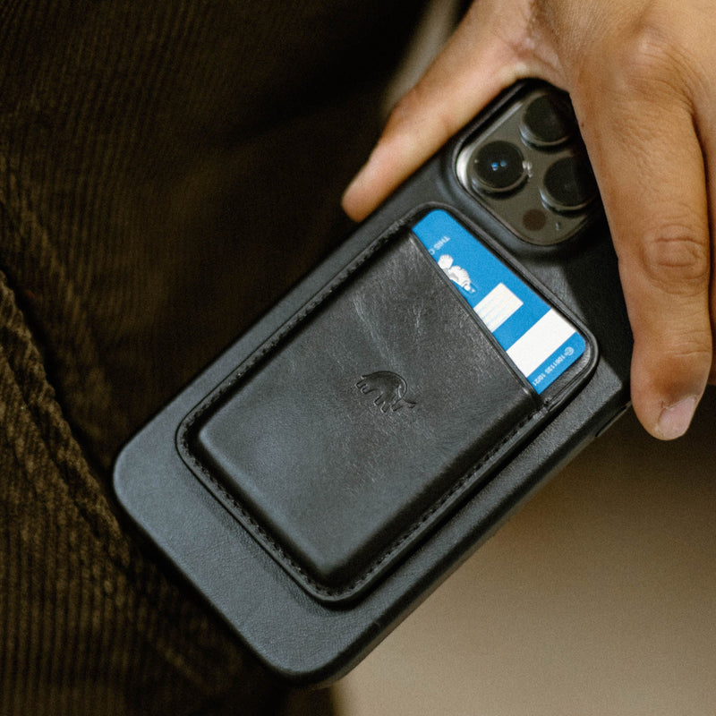 Black leather card pocket attached to a phone case with a blue card partially visible and a hand holding the phone