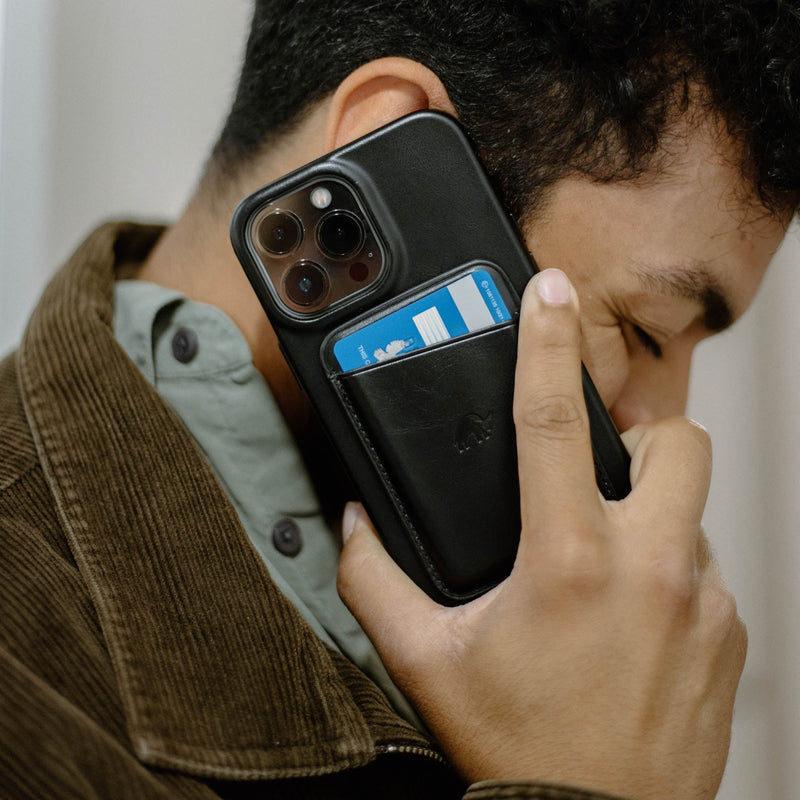 A person holding a black leather magnetic wallet with a card visible