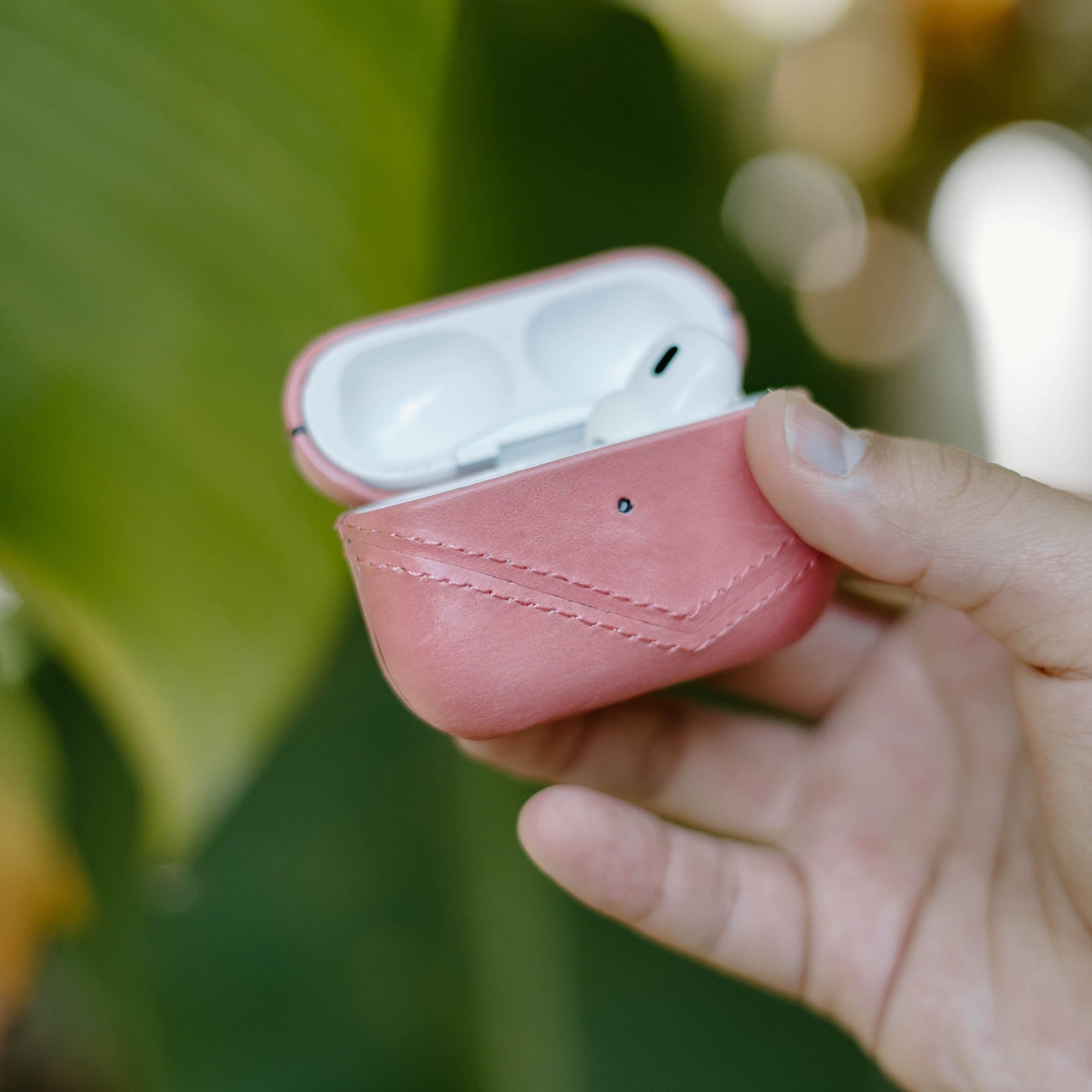 A person holding a pink leather AirPods case with the lid open, revealing the AirPods inside.