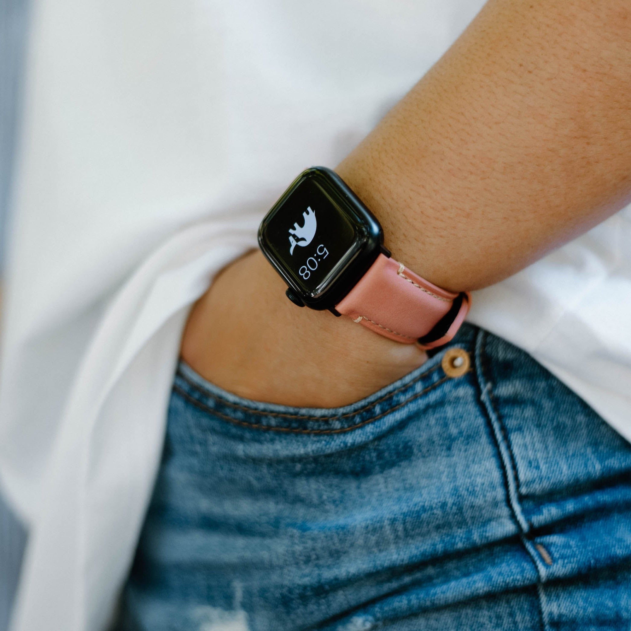 Wrist wearing a square smartwatch with a pink leather band; watch face shows a bird icon and 5:08.