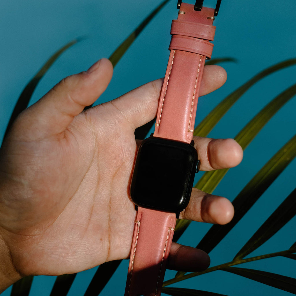 A hand holding a leather Apple Watch strap in Sienna color against a blue background.