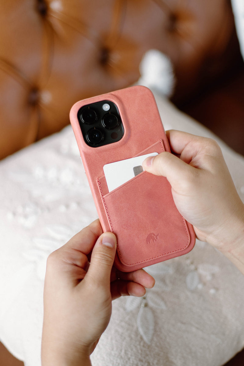 A person holding a pink leather phone case with a card in the back pocket.