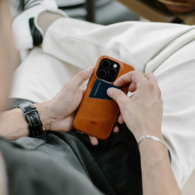 A person holding the Minimalist Portfolio Case in SIENNA color, inserting a card into it.