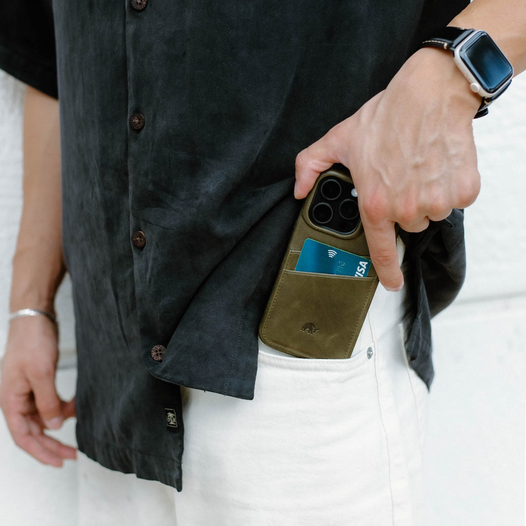 Hand placing phone with MAVERICK minimalist portfolio case and VISA card into white pants pocket