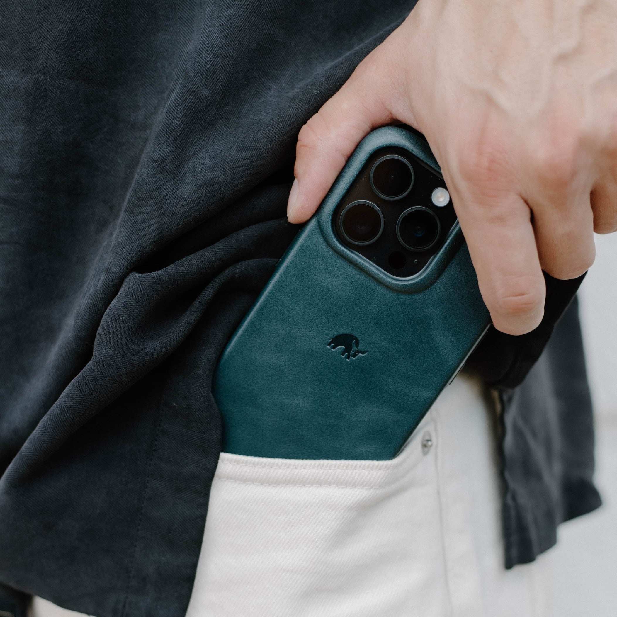 A hand holding the Minimalist iPhone case in ocean color, partially in a pocket.