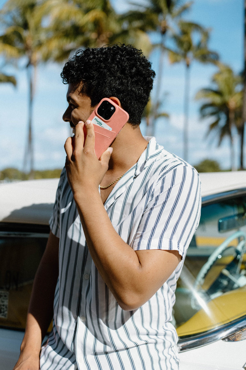 A person wearing a striped shirt holding a phone next to a car with palm trees in the background.