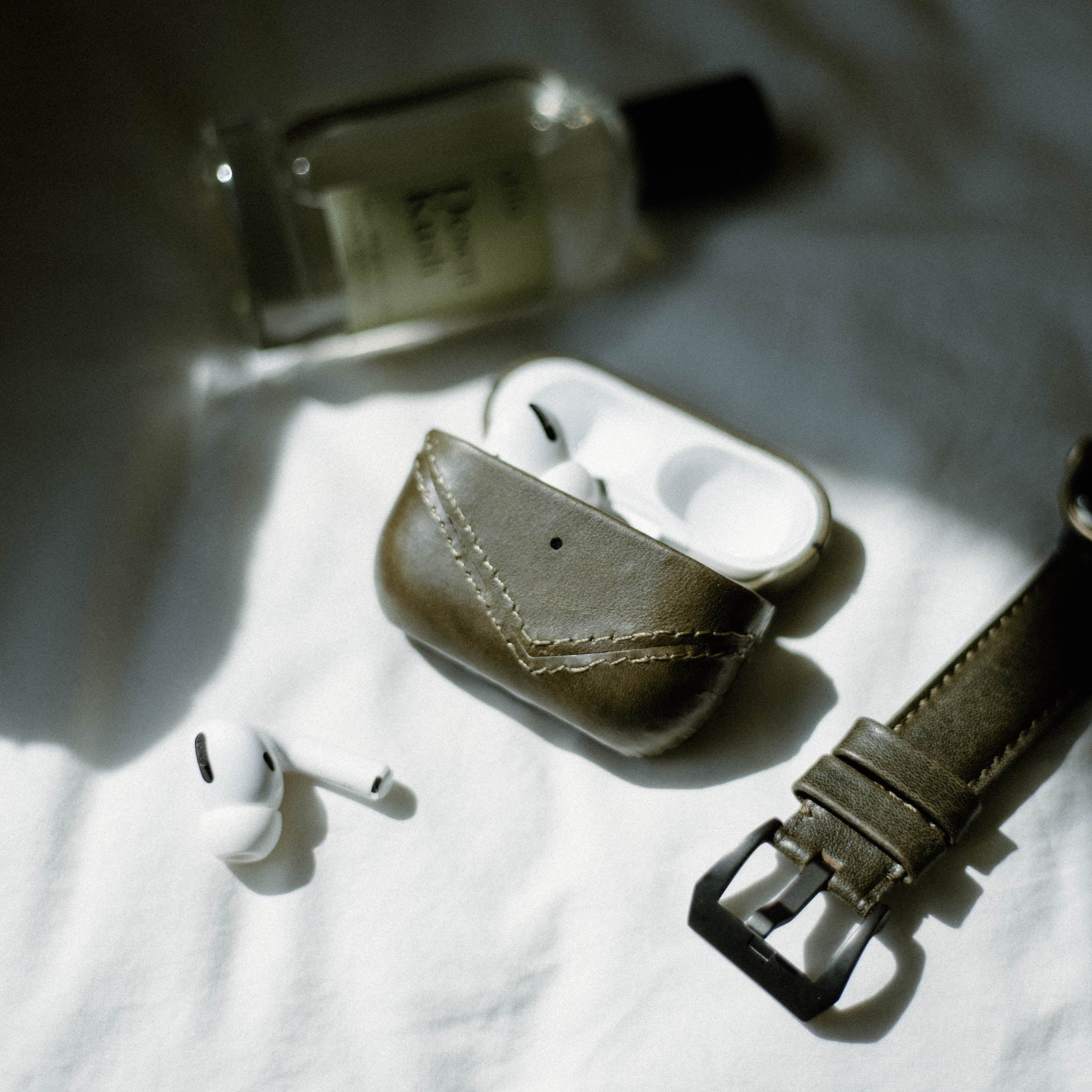 Leather AirPods case in brown with AirPods and a watch on a white surface
