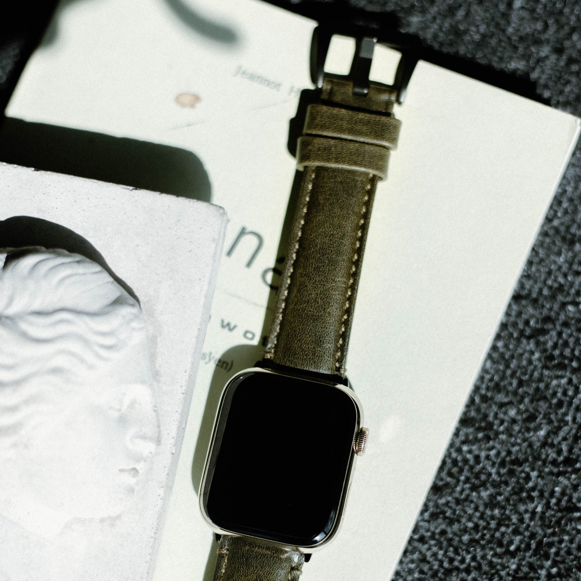 Leather Apple Watch Strap in Maverick color displayed on a book with a sculpture