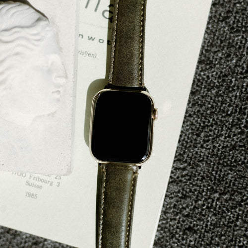 Olive-green leather Apple Watch strap (Maverick) with blank black face on page showing 'Fribourg 3 Suisse 1985'
