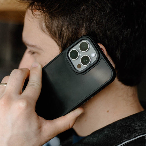 Hand holding phone to ear showing matte black protective case and triple camera lenses