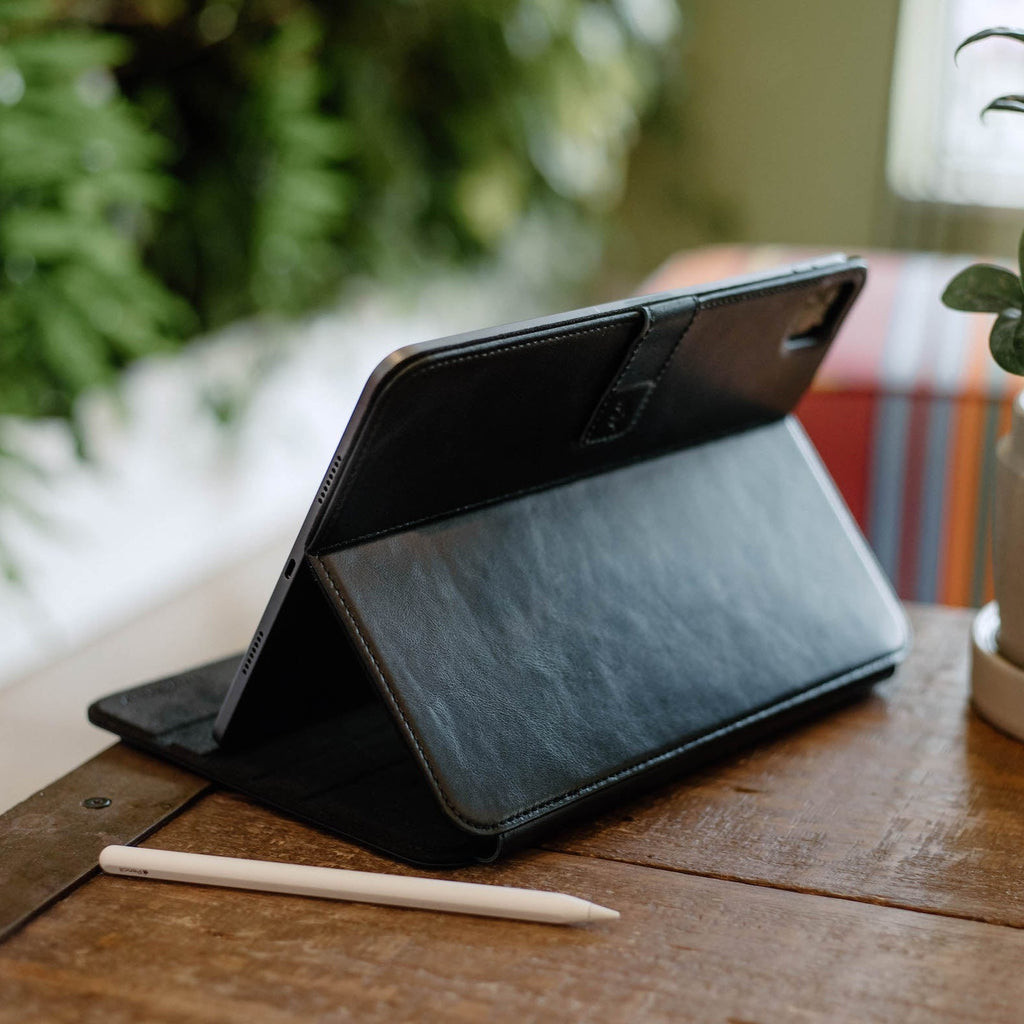Black leather iPad case positioned on a table with a stylus beside it