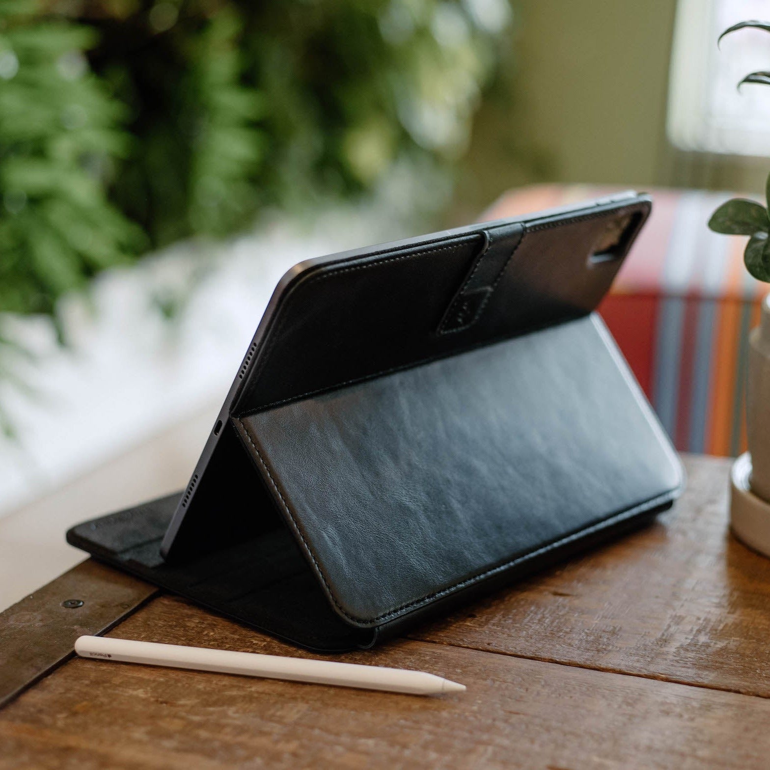 Black leather iPad case positioned on a table with a stylus beside it
