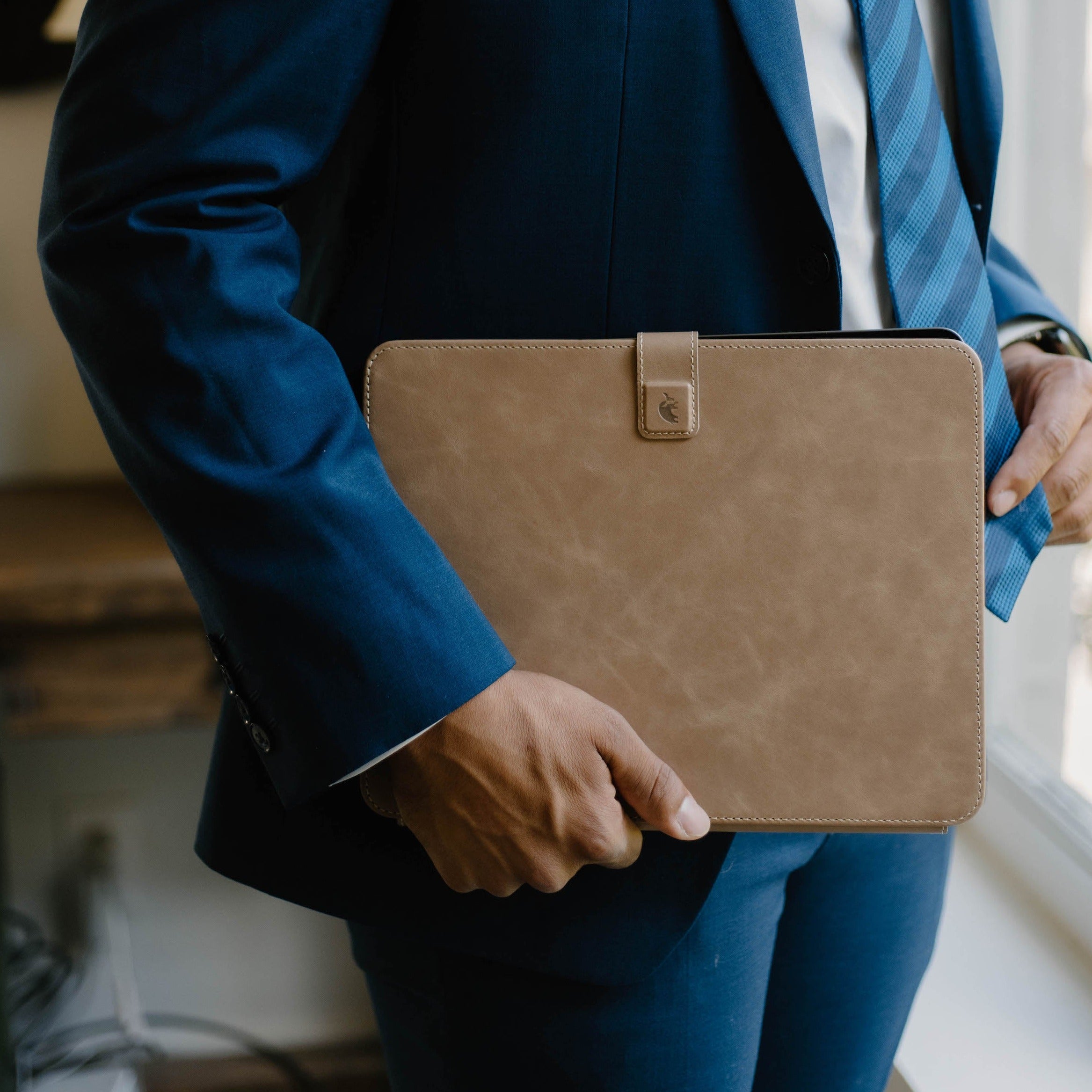A person in a suit holding a tan leather iPad case