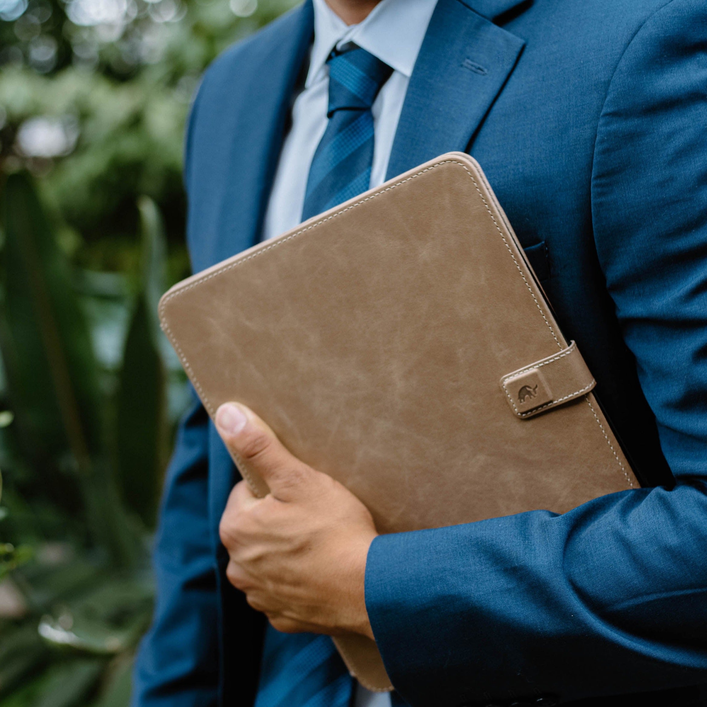 A person in a suit holding a leather iPad case in a natural setting.