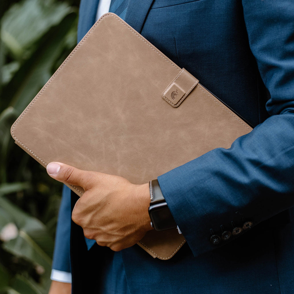 A person in a suit holding a leather iPad case in Dune color.