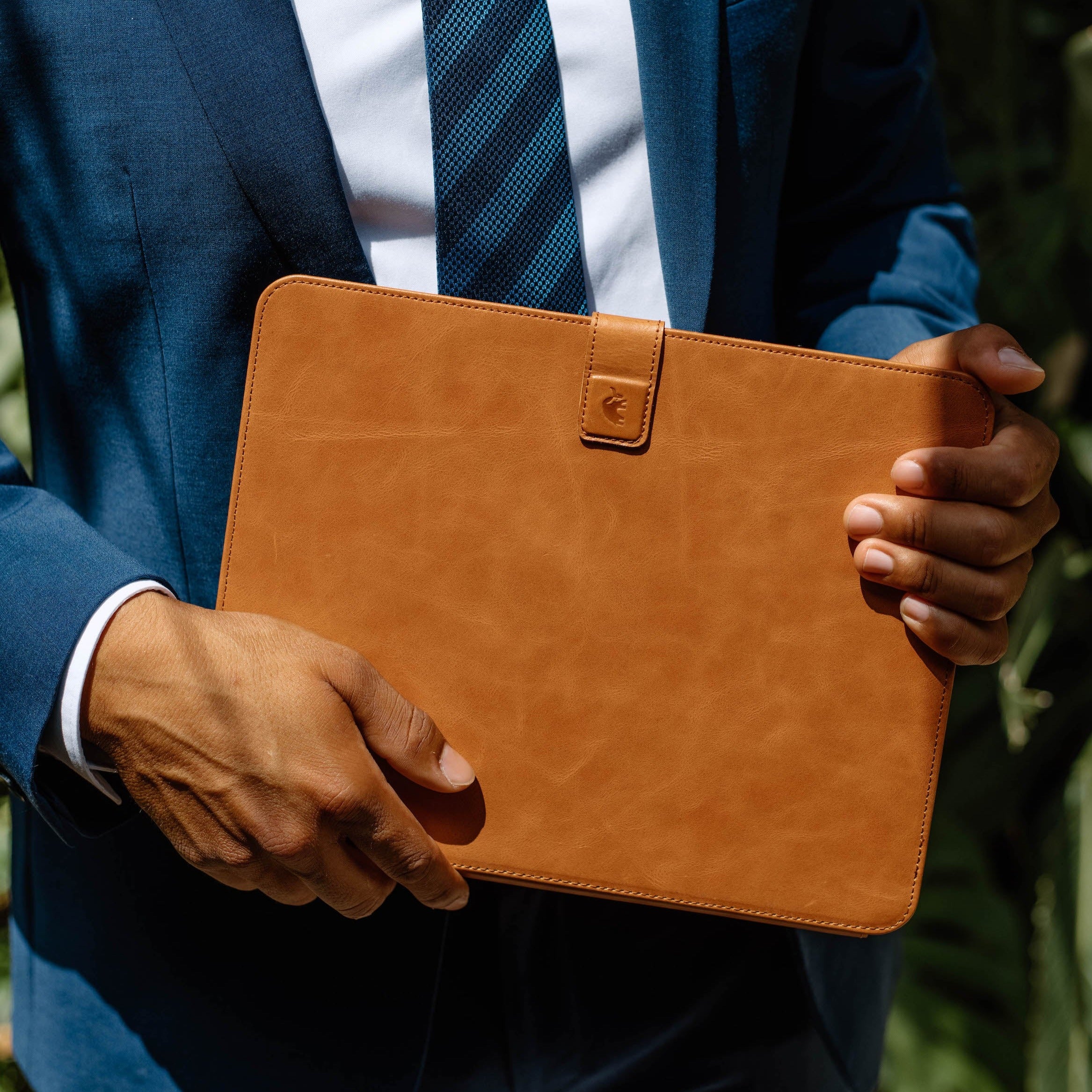 A person in a suit holding a tan leather iPad case, branded SIENNA.