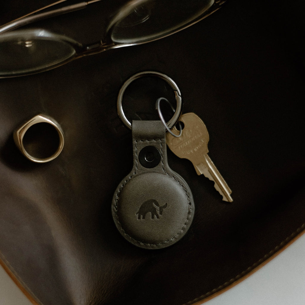 Top-down view of slate BullTag for AirTag leather key fob showcasing embossed bull logo and attached key on dark leather background
