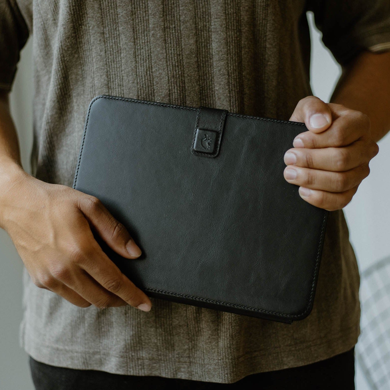 A person holding a black leather iPad case with a button closure.