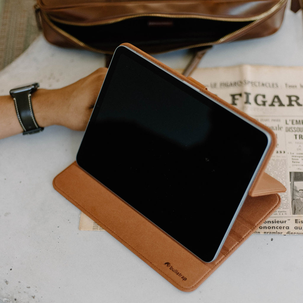 Tablet in tan folio case resting on a newspaper showing 'LE FIGARO SPECTACLES' and 'FIGAR'; case label 'bullstrap' visible.