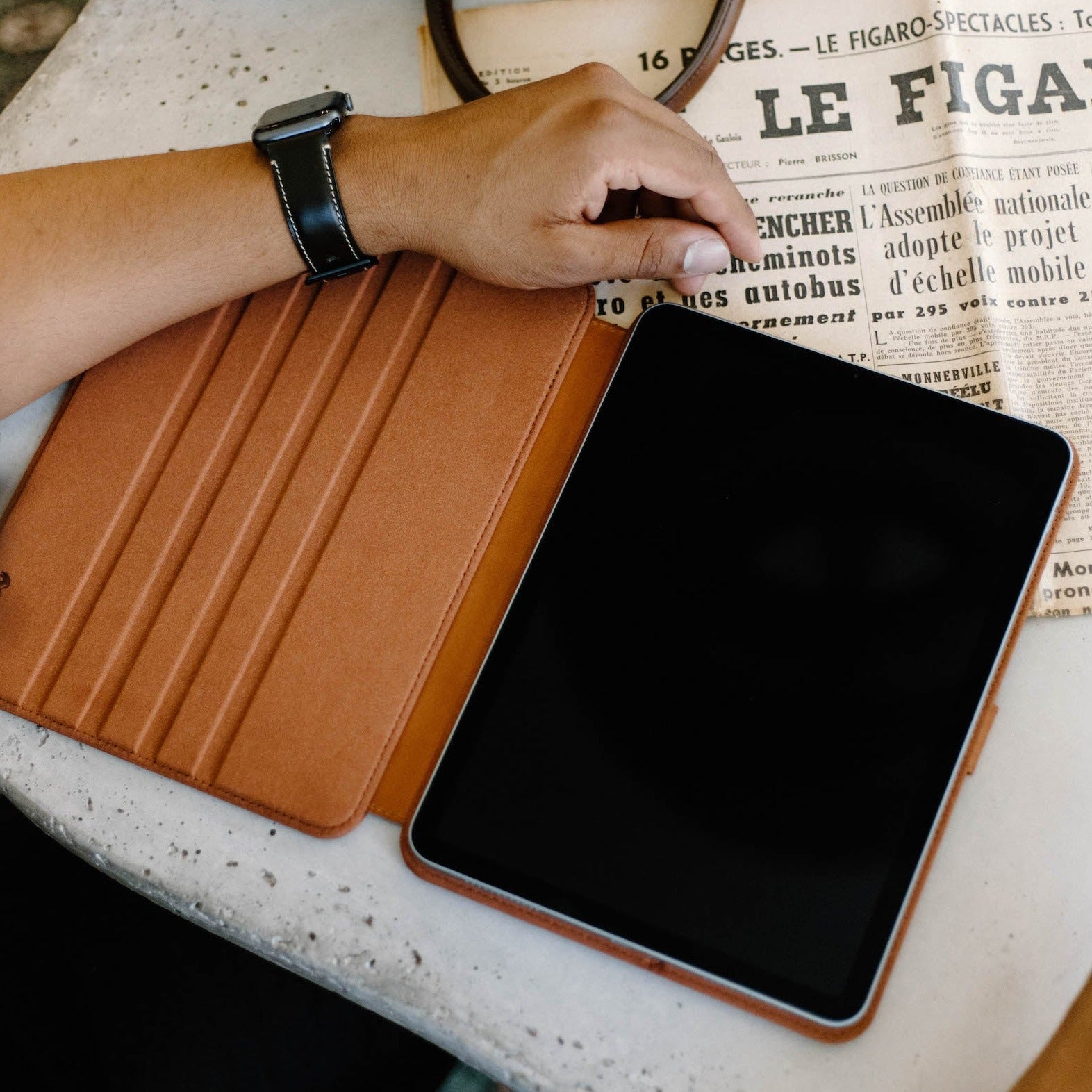 Open sienna leather iPad case with tablet on table over newspaper reading: 16 PAGES - LE FIGARO-SPECTACLES: LE FIGARO