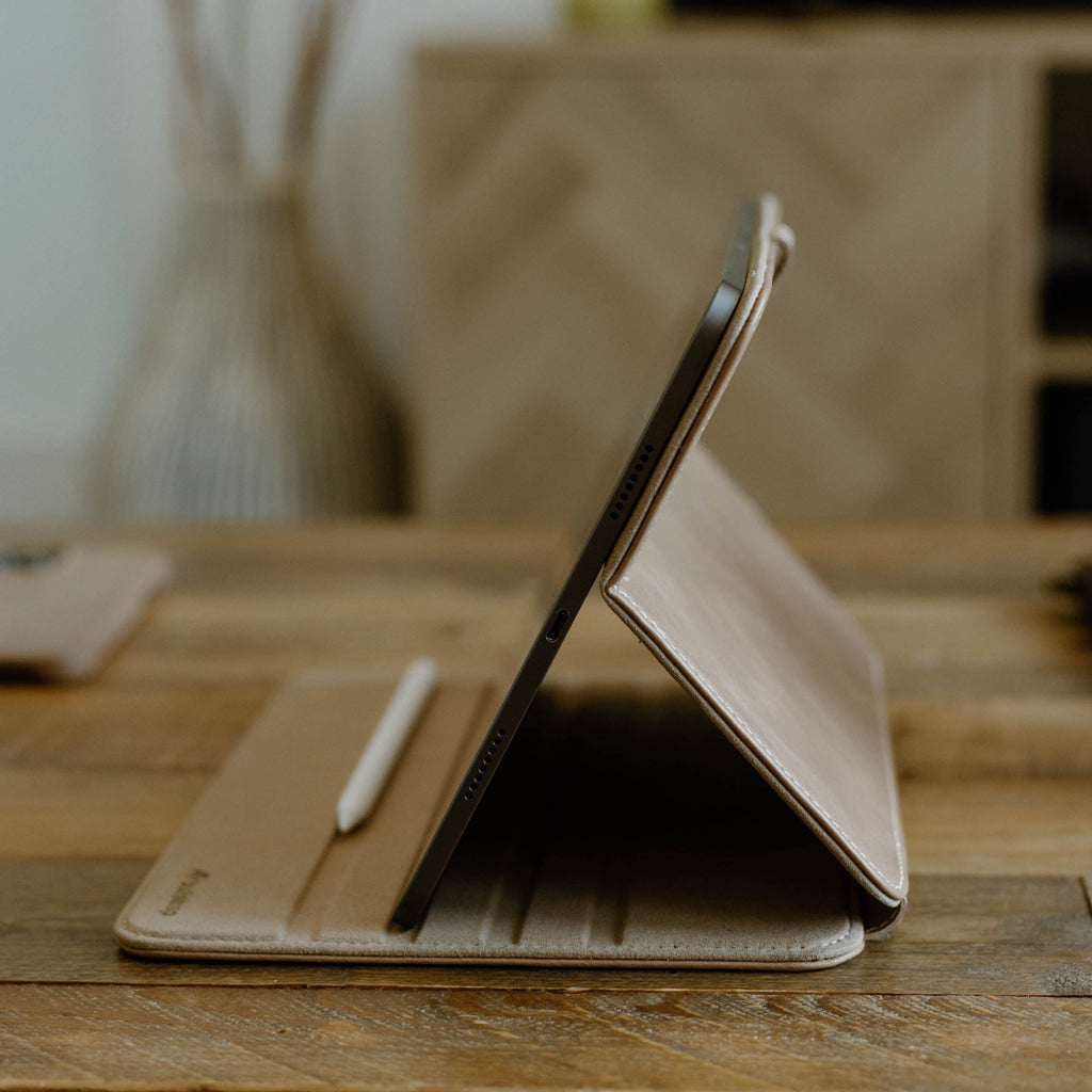 An iPad in a leather case on a wooden table with a stylus beside it.