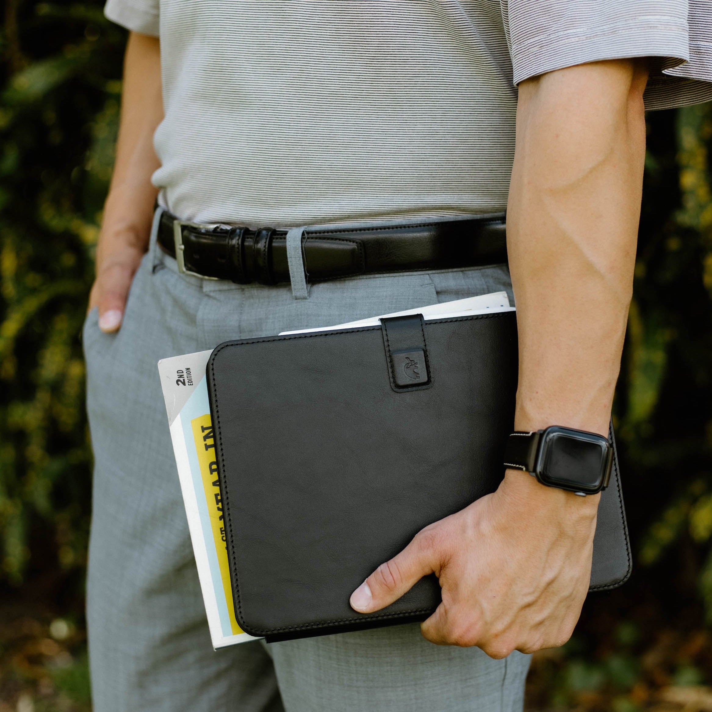A person holding a black leather iPad case with documents in hand.