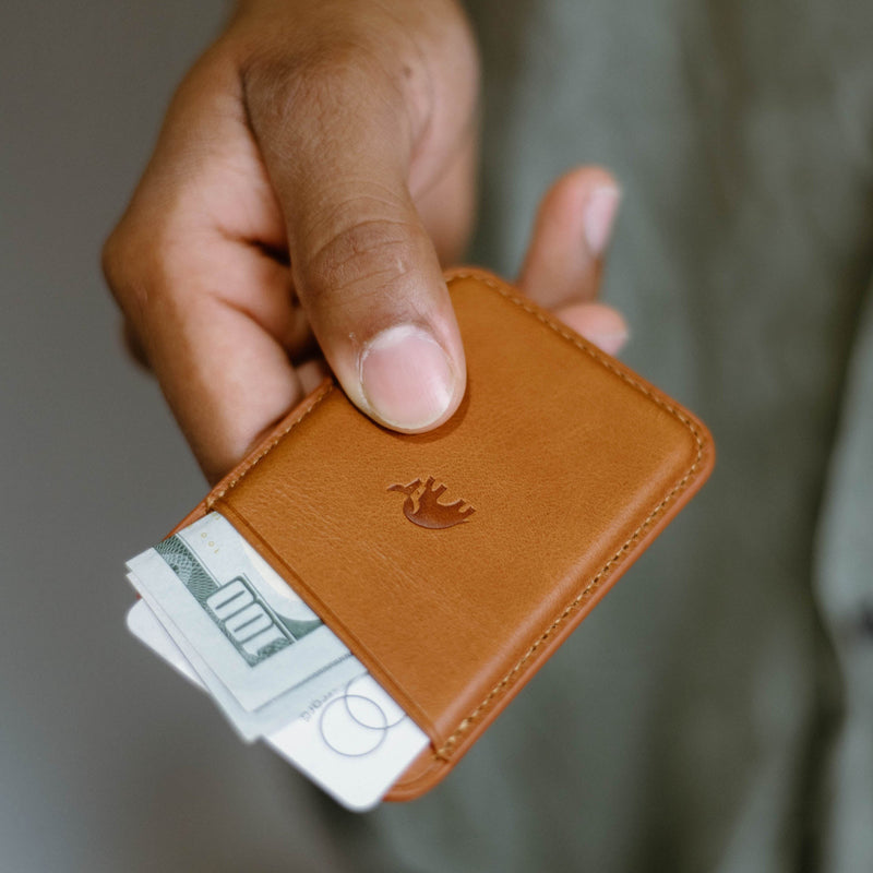A hand holding a leather wallet with cash inside.