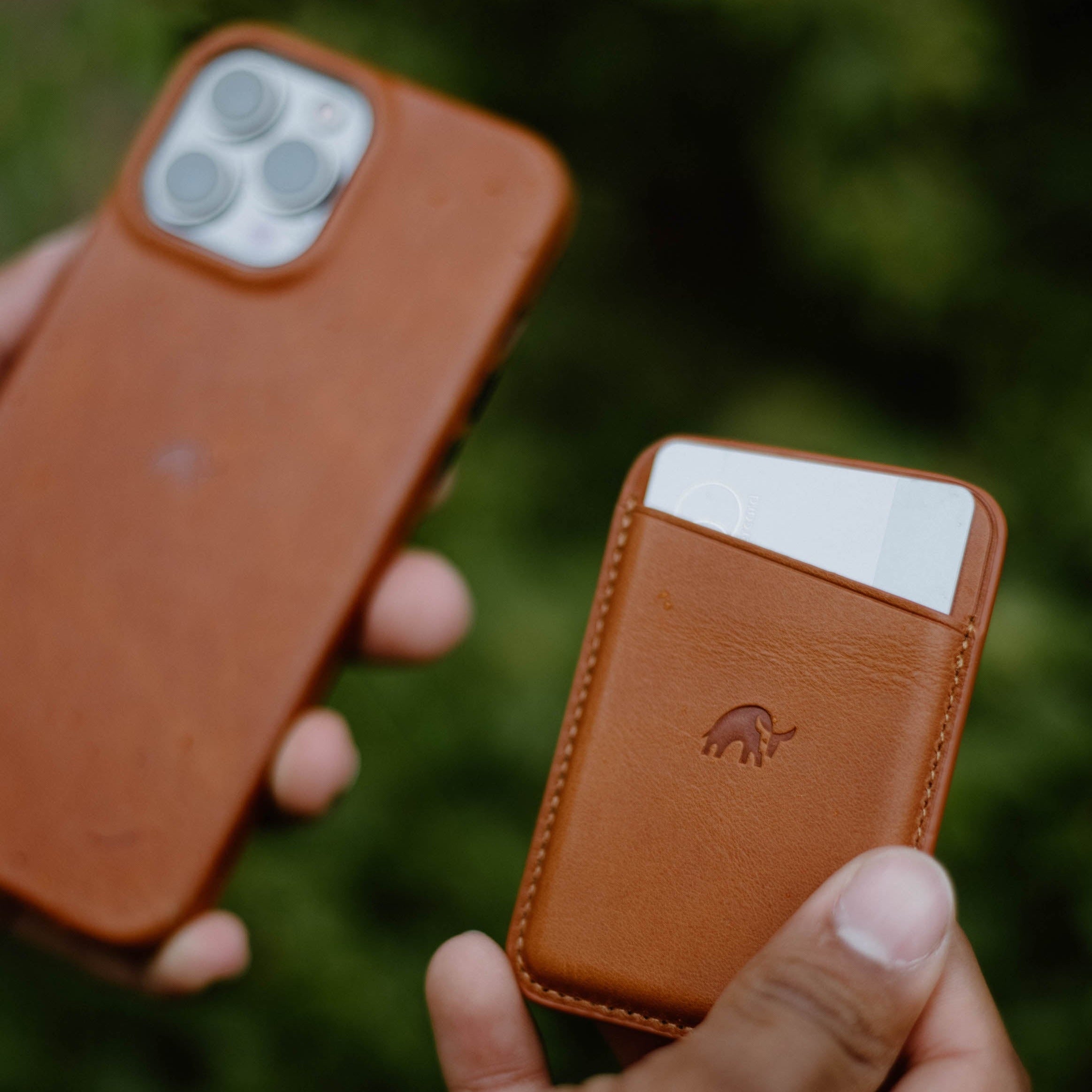 A person holding a brown leather magnetic wallet and a phone case, both in a natural setting.