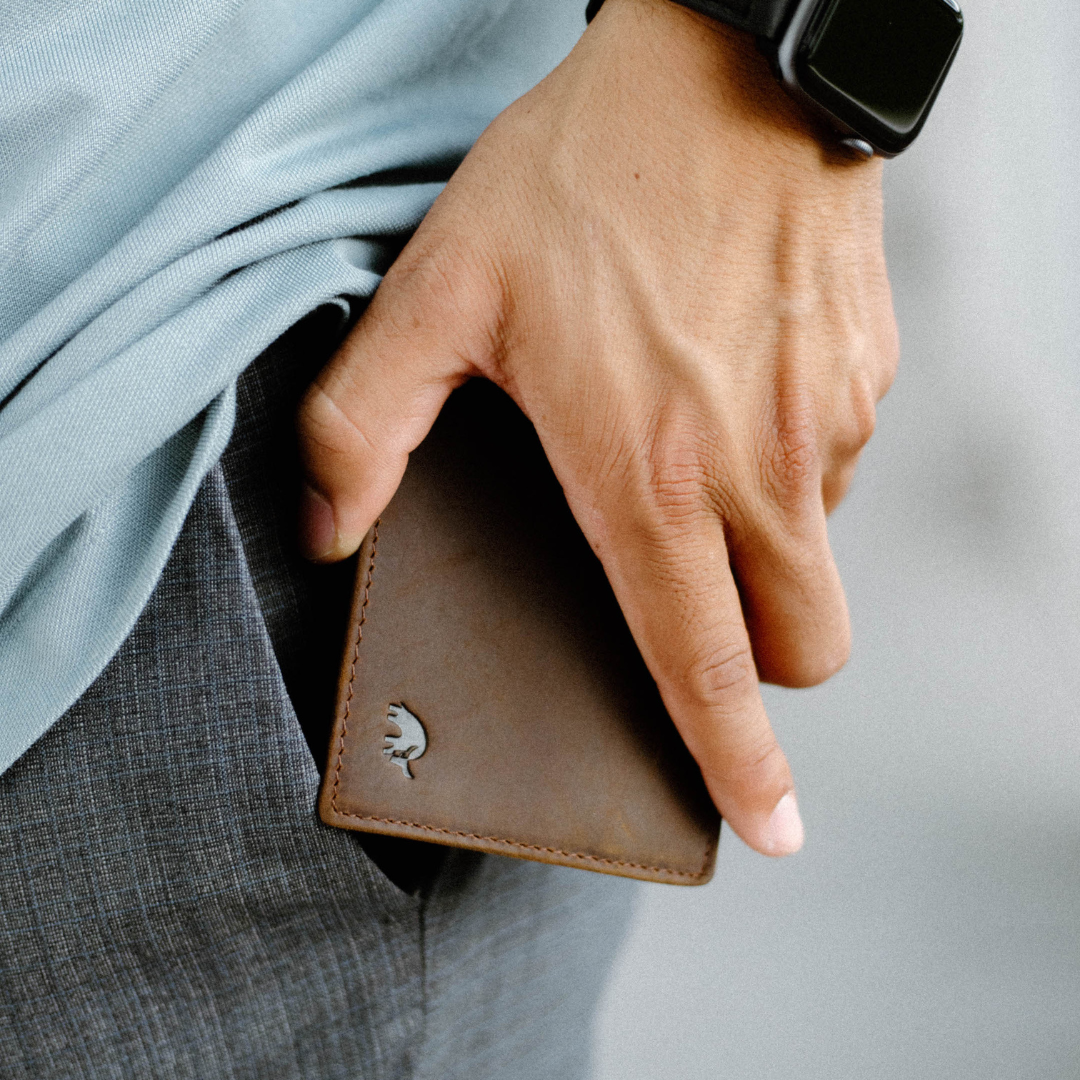 Brown leather bifold wallet held in a hand, embossed logo visible on lower corner.