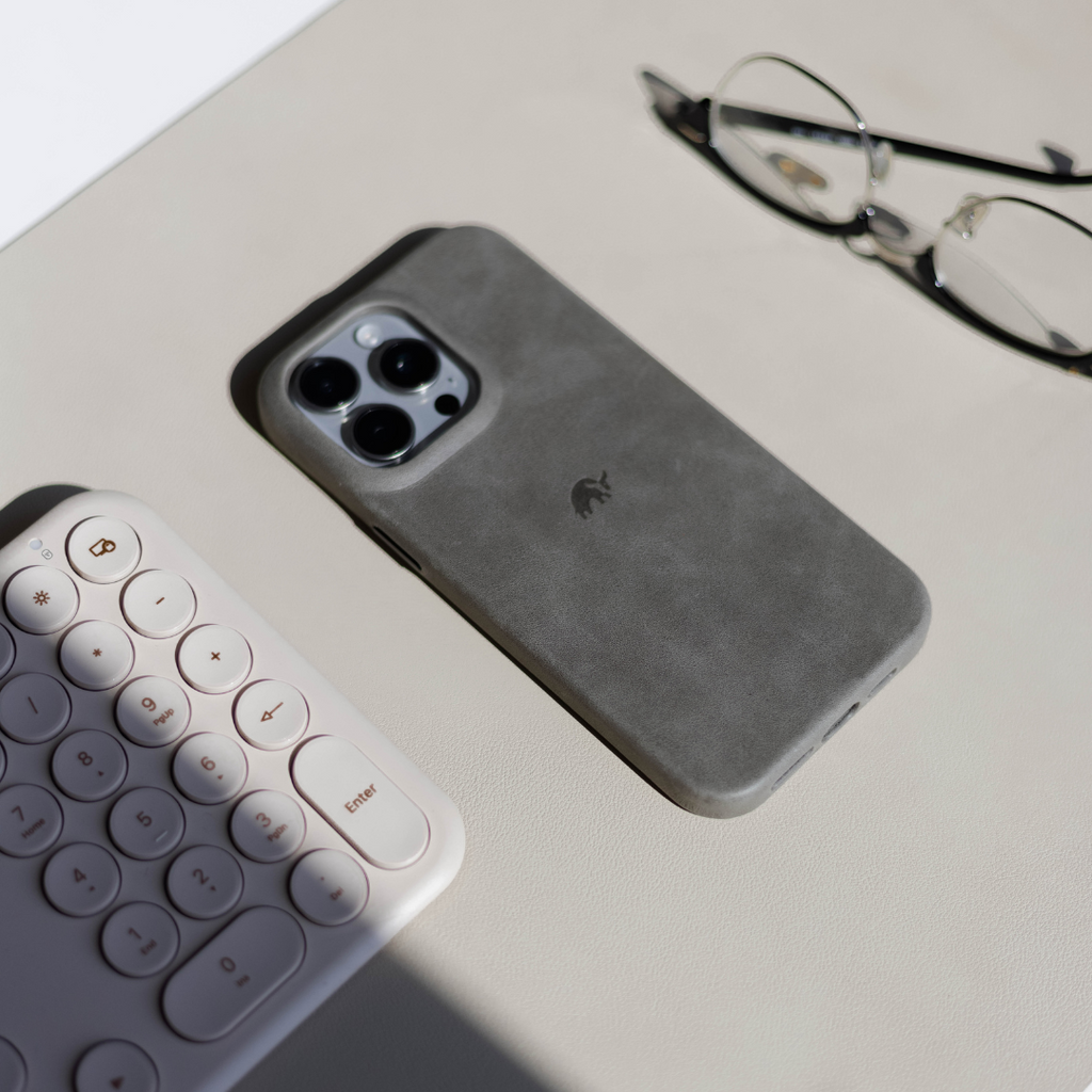 A gray phone case on a desk with a keyboard and glasses