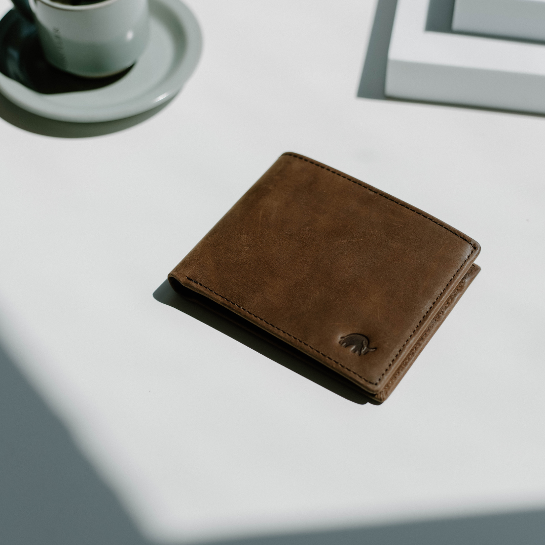 Brown bifold wallet on a table with a coffee cup and books