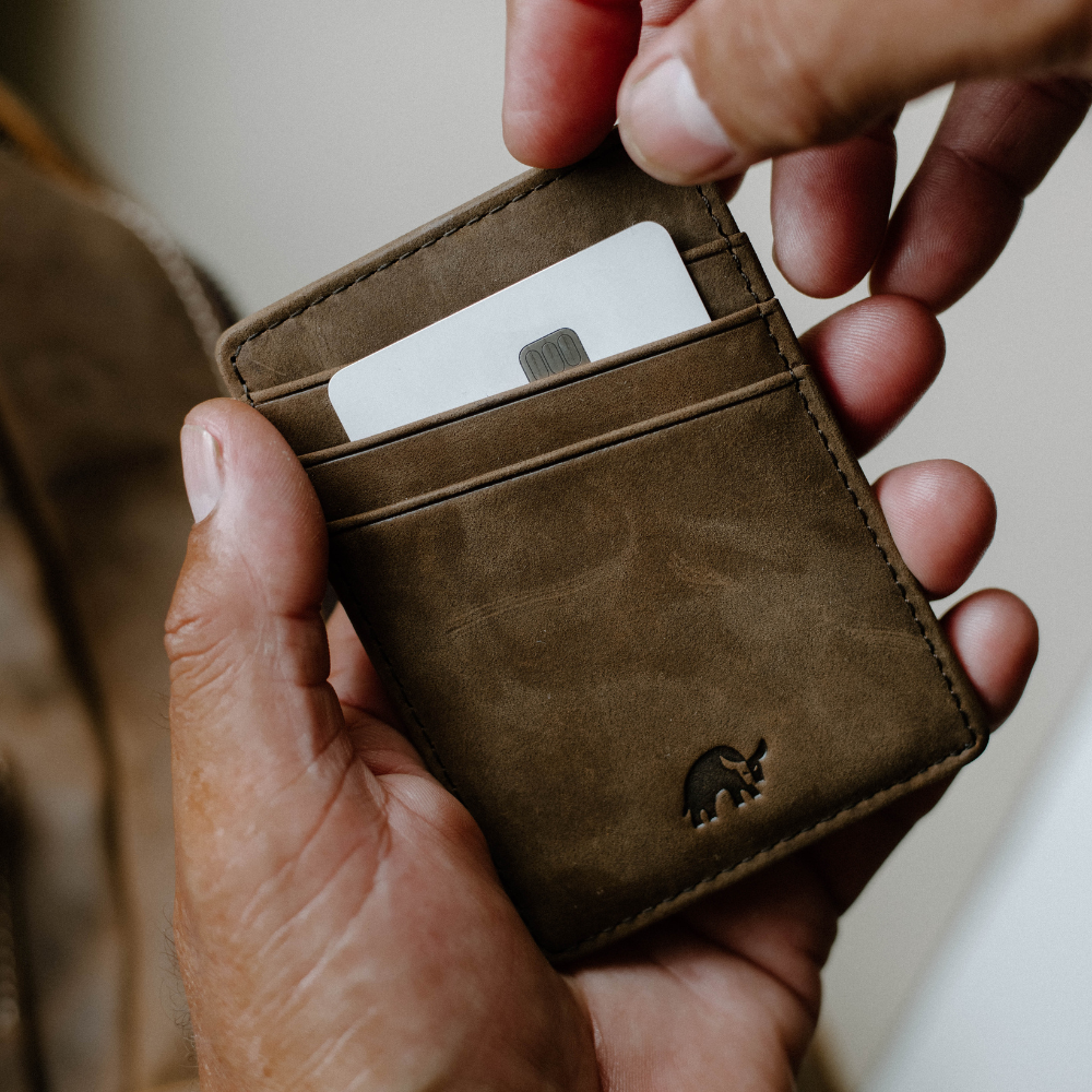 A person holding a brown wallet with a card partially inserted.