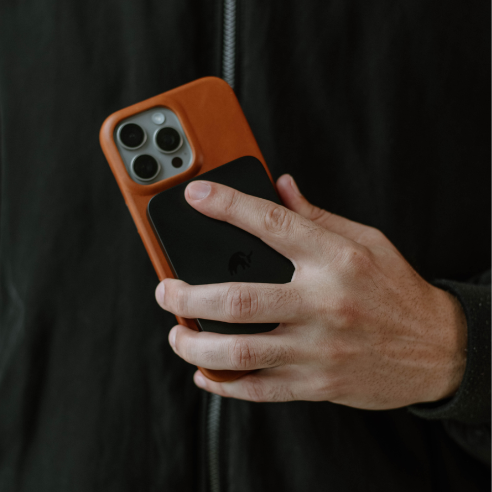 A person holding an iPhone with a MagSafe Power Bank attached to it.