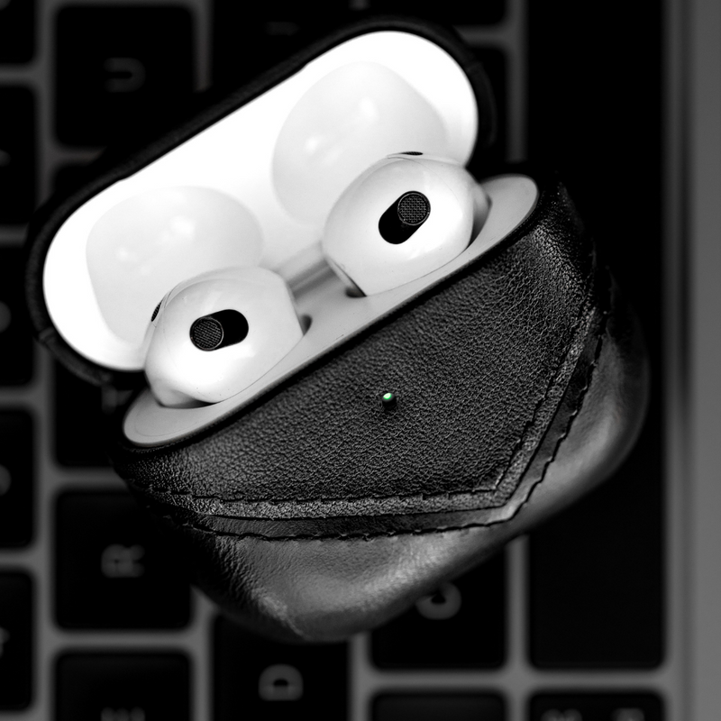 Black leather AirPods case with AirPods inside, showing charging light.