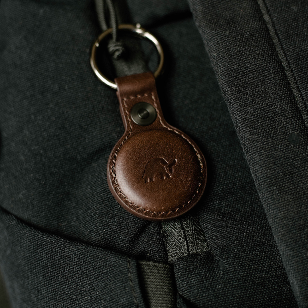 Brown leather AirTag keyring with embossed bull logo attached to dark fabric backpack