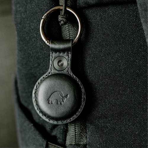 Black leather round key fob with embossed ox logo hanging from a metal key ring on dark textured fabric.