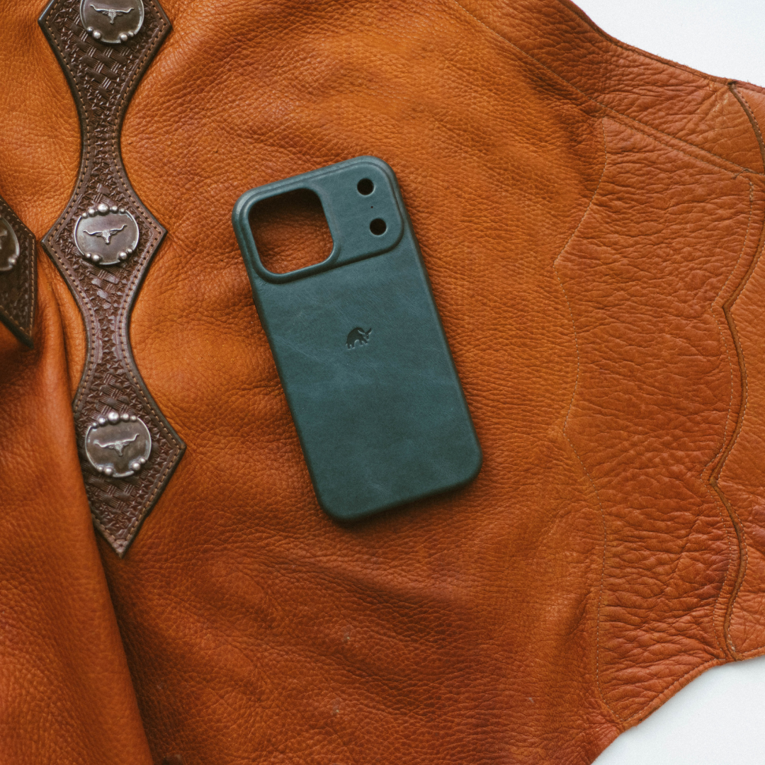 Teal phone case with Bullstrap logo resting on worn brown leather saddle with decorative silver conchos