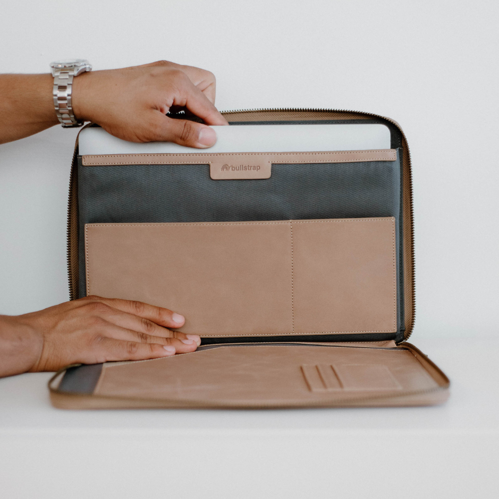 A person holding a leather MacBook sleeve open, showing its interior compartments.