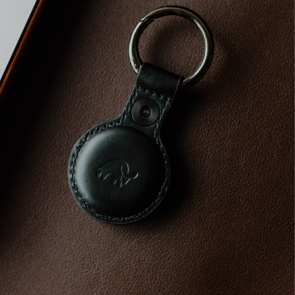 Black leather AirTag keyring with embossed bull logo on brown leather surface